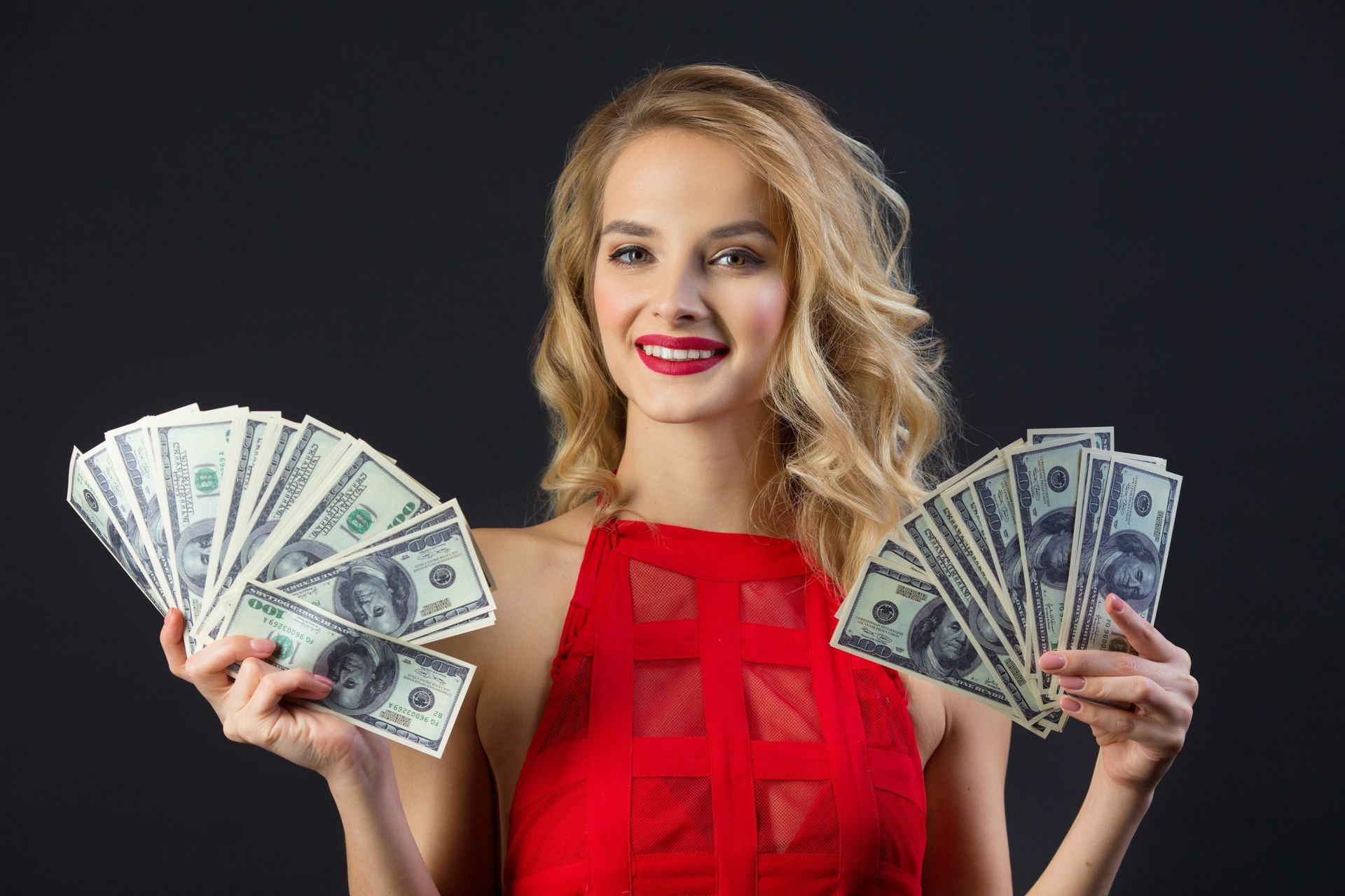 beautiful young girl with hairstyle and makeup in a red dress holding dollars in her hands